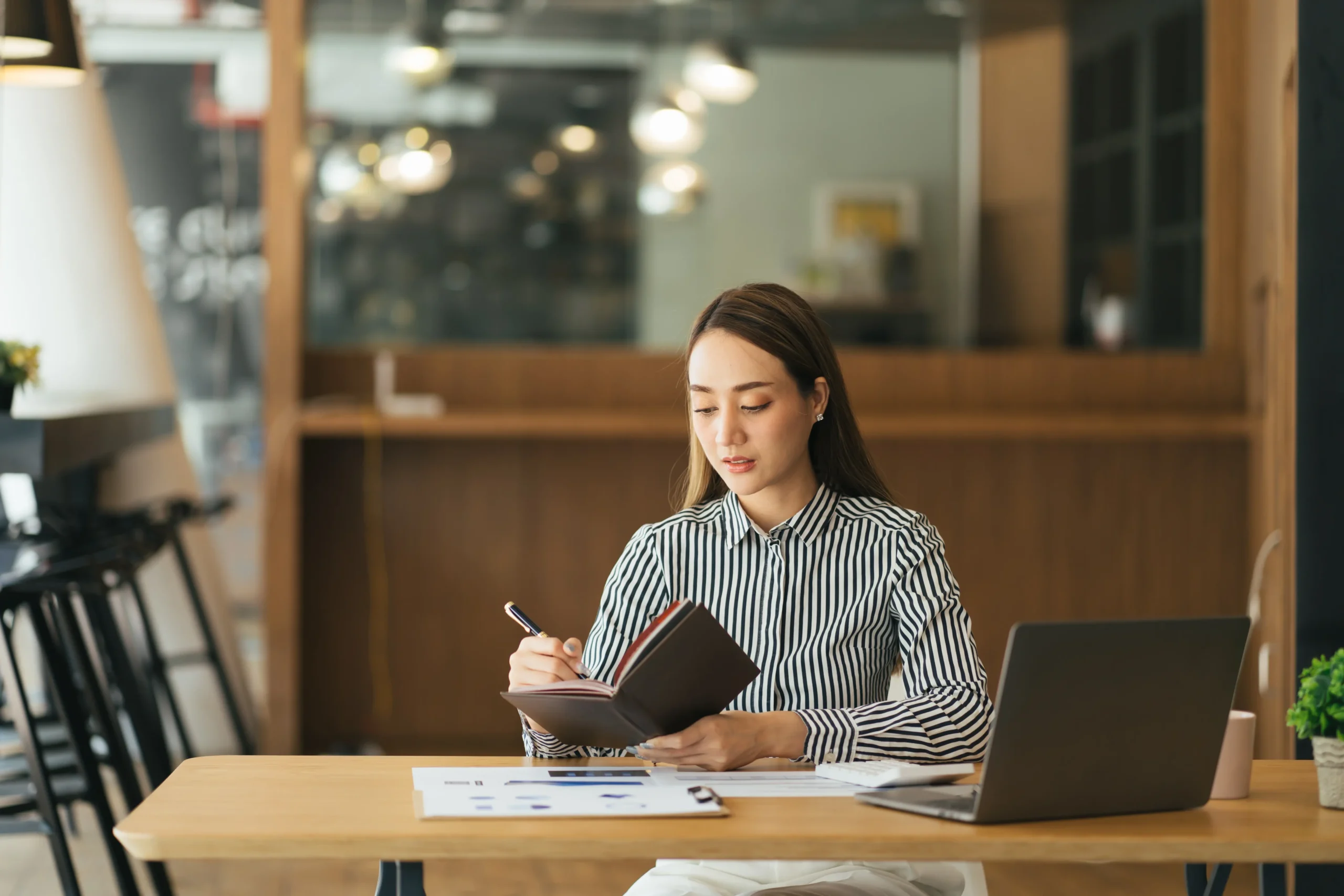 Assistante administrative pensive vérifiant un rapport sur un ordinateur portable lisant des informations et notant des données